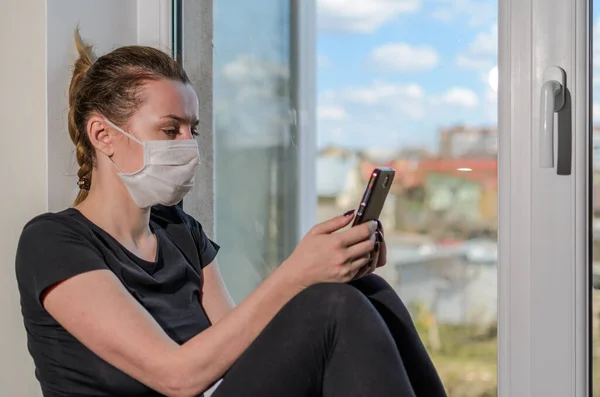 Young Girl Medical Mask Sits Windowsill Window Looks Smartphone — Stock Photo, Image