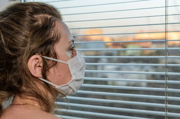 Young Woman Medical Mask Looks Out Window Blinds — Stock Photo, Image