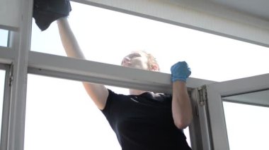 Genç bir kadın pencereyi paçavrayla temizliyor.