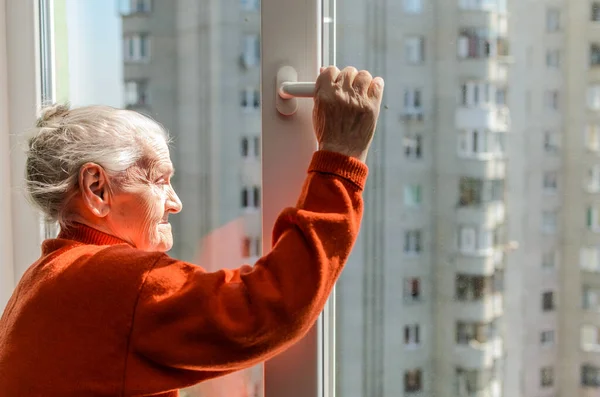 An elderly woman opens a window on a sunny day