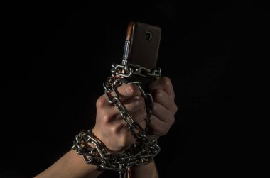 Siyah arka planda akıllı bir telefonla zincirlenmiş insan elleri.