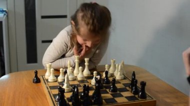 Küçük kız annesiyle satranç oynuyor.