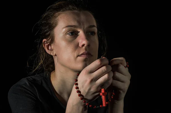 Young woman praying to god with prayer beads with a crucifix on the cross