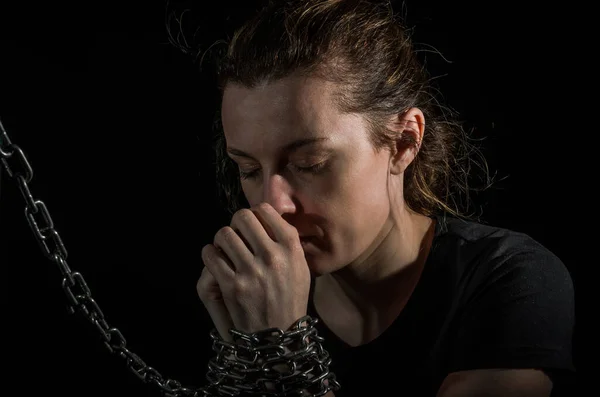 Young woman blindfolded in chains breaks out of them on a black background