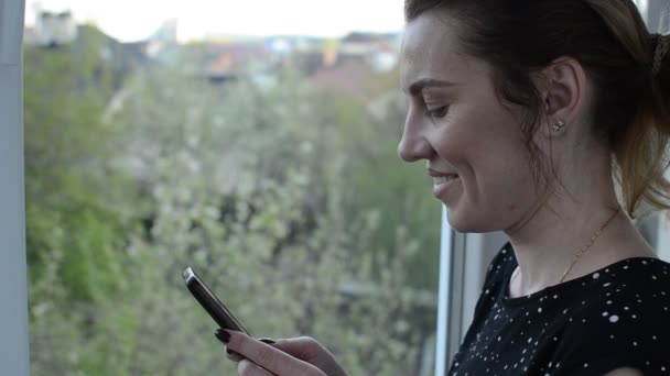 Mujer Joven Cerca Ventana Comunica Mensajero Teléfono Inteligente — Vídeo de stock