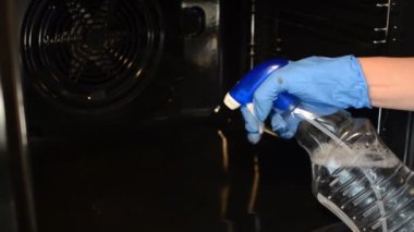 Eldivenli bir hizmetçi elektrikli fırını bez ve temizlik maddesiyle yıkıyor.