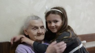 Küçük sevimli kız torun yaşlı bir büyükanneye sarılıyor.