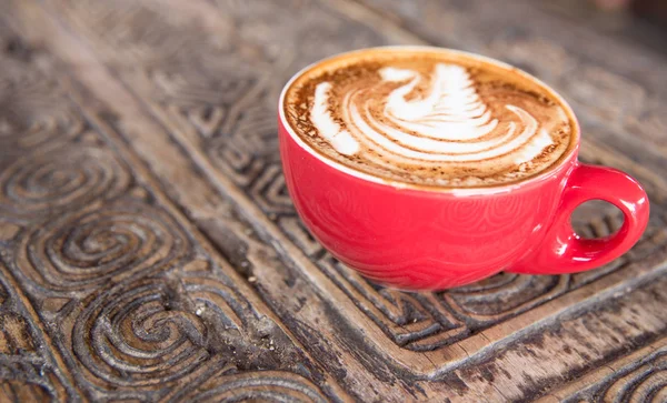 Cup of tasty cappuccino is on the wooden textured table in red c — Stock Photo, Image