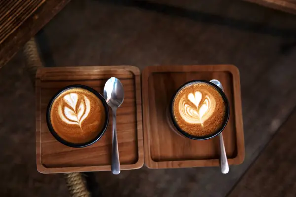 两杯热卡布奇诺咖啡放在木制桌子上 汤匙放在玻璃桌子的背景上 早餐时间 顶部视图 — 图库照片