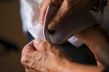 Damadın annesi kol düğmesi ve gömlek takarak hazırlanmasına yardım ediyor.