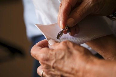 Damadın annesi kol düğmesi ve gömlek takarak hazırlanmasına yardım ediyor.
