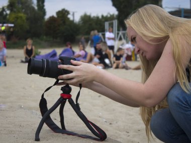 Kız videocu, şehir plajındaki bir nehrin kıyısında hikaye yazıyor. Kamerası tripodun üzerinde..