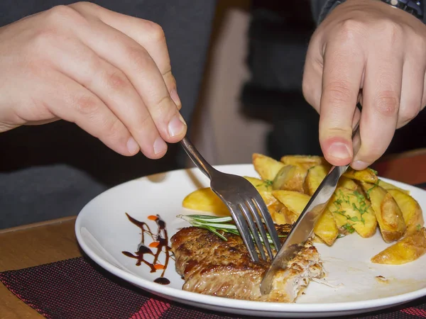 Cips ve biftek, üstünde biberiye filizi olan bir kafede beyaz bir tabakta. Çatal ve bıçaklı bir adamın elleri..