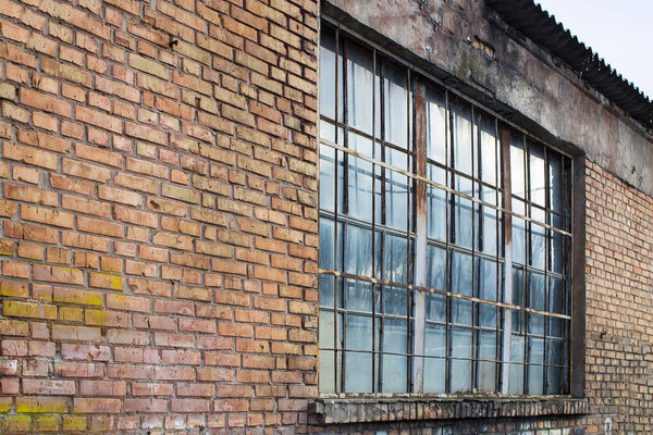 Large window in an old red brick building. In front of the window is a metal grill, covered with rust.