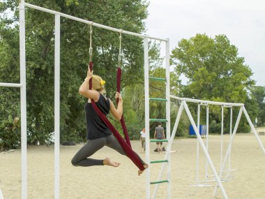 Doğada, deniz kıyısında uçan yoga dersleri. Şehir plajında bir hamakta, bir antrenörle yoga eğitimi alan güzel bir kız..