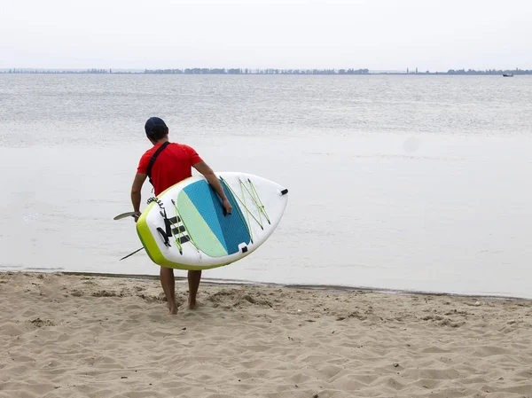 Water sports, surfing. A man with a board in his hands goes to sea. Active holiday, weekend at sea.