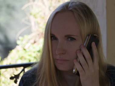 Sarışın kız telefonda konuşuyor. Pencerenin kenarında oturuyor..