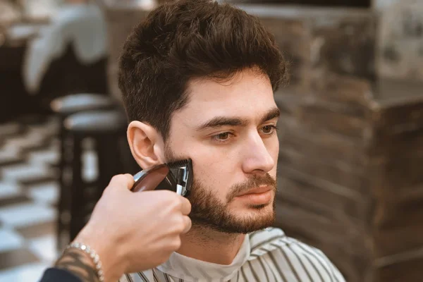 As mãos de barbeiro jovem fazendo corte de cabelo para homem atraente na barbearia — Fotografia de Stock