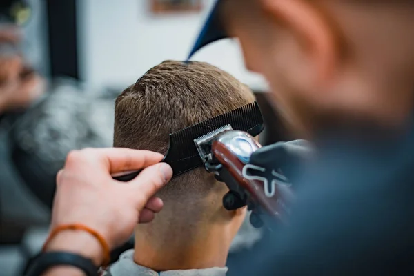 Man gets a cool haircut in barbershop. Barber makes the cut man electric razor. Men\'s care head. Soft focus.