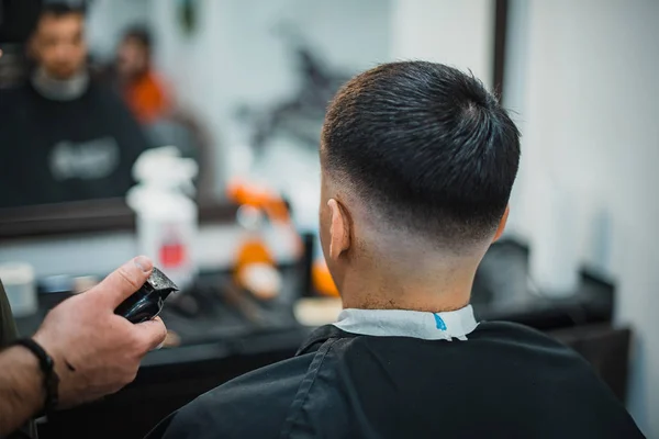 O homem tem um corte de cabelo fixe na barbearia. O barbeiro faz a navalha eléctrica do homem do corte. Cabeça de homem. Foco suave . — Fotografia de Stock