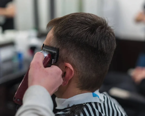 Les mains du jeune coiffeur faisant coupe de cheveux à l'homme attrayant dans le salon de coiffure — Photo