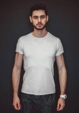 Beyaz t-shirt giyen bir gülümseyen yakışıklı genç portresi. Stüdyo koyu arka plan üzerinde vurdu. Erkek güzellik ve sağlık.