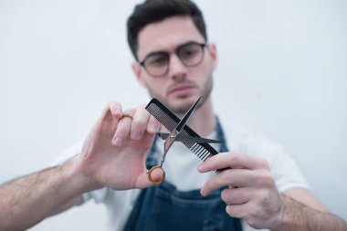Bir sakallı bir adam görüntüsü. Holding Model makas Kuaför ve hafif bir arka plan üzerine tarak. Ellerini üstüne odaklanmak.