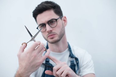 adam kısa bir saç kesimi ile bir gülümseme ile genç tutan makas bir açık renkli portre Kuaför. Ellerini üstüne odaklanmak.