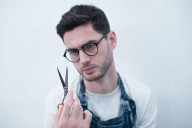 Arka planı beyaz bir duvar uzun ellerinde makas Kuaför tutar.