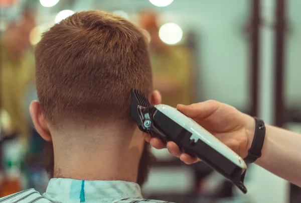 Penteado masculino e corte de cabelo com cortador de cabelo em uma barbearia ou salão de cabeleireiro. Foco suave . — Fotografia de Stock