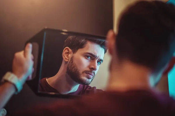 Retrato de um jovem barbudo que olha para si mesmo através do espelho no salão de beleza . — Fotografia de Stock