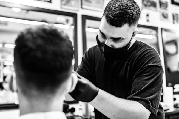Corte de cabelo dos homens em uma barbearia. Cliente e barbeiro em máscaras antivírus . — Fotografia de Stock