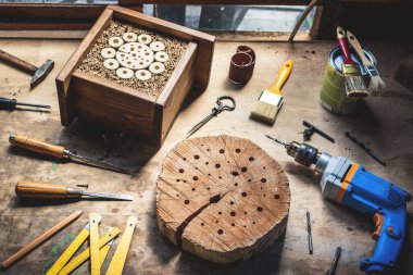 Ahşap böcek oteli ya da atölyede ev yapmak. DIY ve iş aletleri masada. Matkap, keski, boya fırçası, çekiç ve dekoratif el işi ürünü.