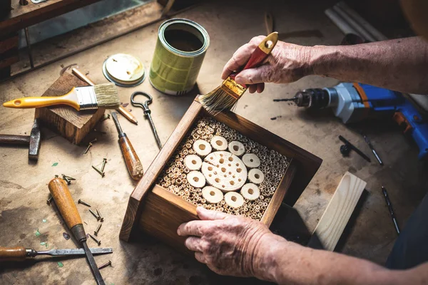 Craftsperson atölyedeki ahşap böcek otelini boyuyor. İnsan yapımı el işi ürünü. Dekoratif böcek evi. Çalışma yeri