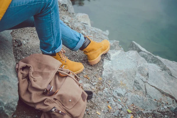 Gambe femminili in jeans e scarponi da trekking vicino al bordo del lago di montagna . — Foto Stock