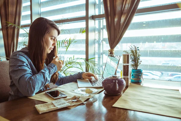Nainen juo teetä kahvilassa ja työskentelee — kuvapankkivalokuva