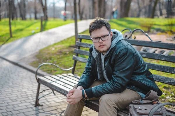 Jonge man in glazen zit op een bankje — Stockfoto