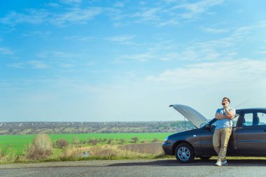 Kızgın genç adam kırık araba yanında otururken bir yardım bekliyor