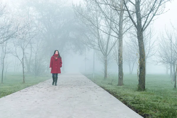 Молода жінка в червоній прогулянці міським парком в тумані — стокове фото