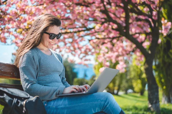 Young beautiful brunette student sit on the banch with laptop — Stock Photo, Image