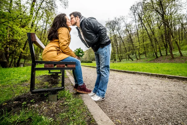 Homem e mulher abraçando e beijando no banco no parque de mola verde — Fotografia de Stock