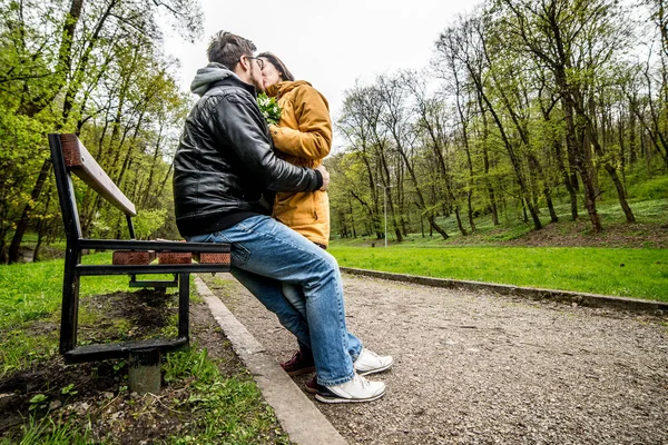 Άνδρας και γυναίκα αγκαλιάζει και φιλιά στον πάγκο στο πάρκο πράσινο άνοιξη — Φωτογραφία Αρχείου