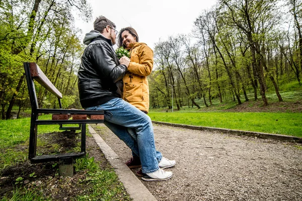 Man and woman embracing and kissing on bench in green spring park — Stock Photo, Image