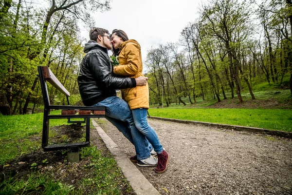 Man and woman embracing and kissing on bench in green spring park — Stock Photo, Image