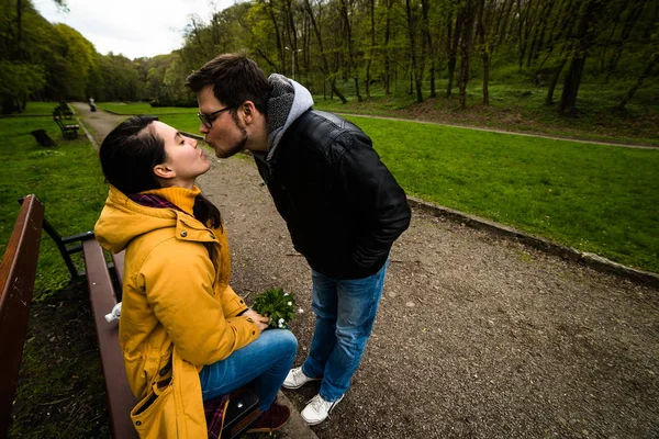 Man och kvinna omfamnar och kysser på bänken i gröna våren park — Stockfoto