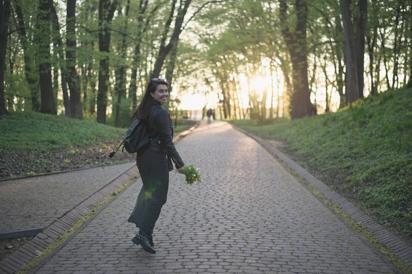 Mulher andando pelo parque com flores nas mãos — Fotografia de Stock