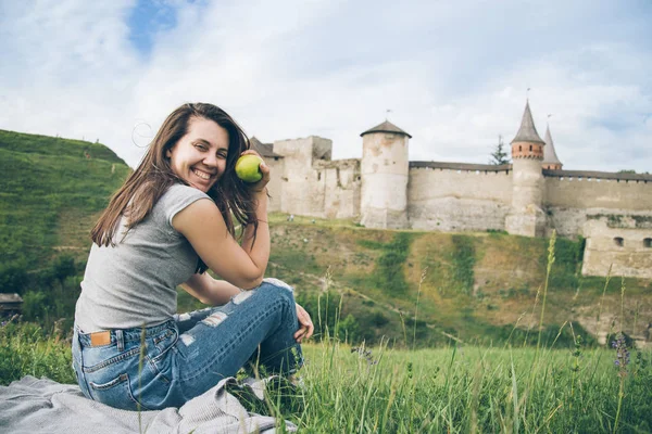 Destul de turist stă pe stâncă în fața castelului vechi și mănâncă aplle — Fotografie, imagine de stoc