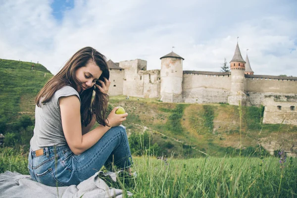 Hübsche Touristin sitzt auf Felsen vor altem Schloss und isst Aplle — Stockfoto