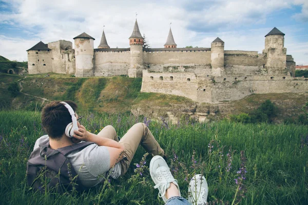 Человек с наушниками лежит на земле и смотрит на старый замок — стоковое фото