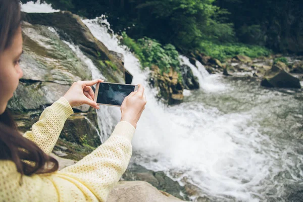 Woman taking picture on the phone of waterfall on background — Stock Photo, Image